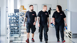 Drei Mitarbeiter gehen durch Produktionshalle und tauschen sich aus