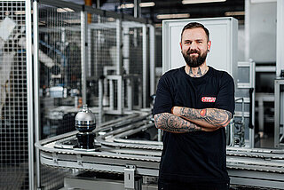 Mitarbeiter steht vor einer automatisierten Produktionsanlage mit Förderband